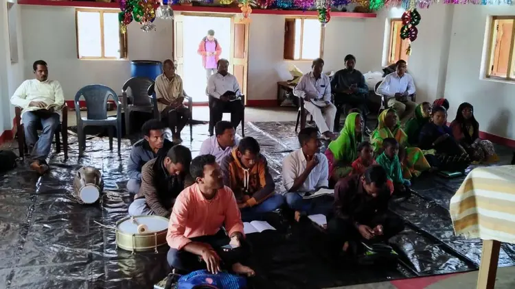group of men, women and children sitting on the floor in a public meeting